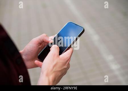Unrecognizable man in red shirt using a modern mobile smartphone in the hands on the outdoors, 5g internet, text messages, video calls Stock Photo