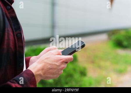 Unrecognizable man in red shirt using a modern mobile smartphone in the hands on the outdoors, 5g internet, text messages, video calls Stock Photo