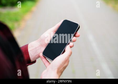 Unrecognizable man in red shirt using a modern mobile smartphone in the hands on the outdoors, 5g internet, text messages, video calls Stock Photo