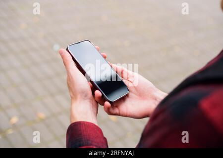 Unrecognizable man in red shirt using a modern mobile smartphone in the hands on the outdoors, 5g internet, text messages, video calls Stock Photo
