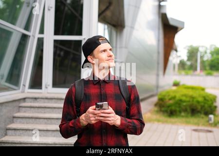 Casual young urban man tourist using a modern smartphone while walking along the city street in the city outdoors, Lifestyle and technology, Side View Stock Photo