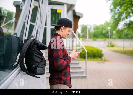 Casual young urban man tourist using a modern smartphone while walking along the city street in the city outdoors, Lifestyle and technology, Side View Stock Photo