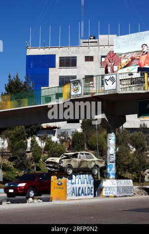 Car driving past crashed car on pedestal in middle of motorway warning drivers not to drink drive and drive carefully, La Ceja, El Alto, Bolivia Stock Photo