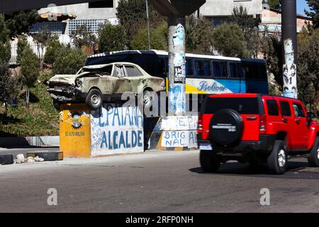 Bolivar bus and red Hummer SUV passing crashed car on pedestal in motorway warning drivers not to drink drive and drive carefully, El Alto, Bolivia Stock Photo