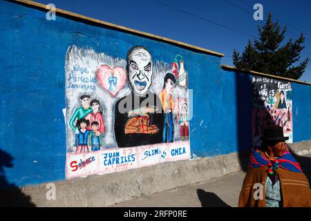 Native Aymara woman walking past a mural that is part of a campaign to reduce domestic abuse and violence against women, El Alto, Bolivia Stock Photo