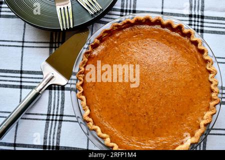 A freshly baked homemade whole pumpkin pie on a black and white plaid tablecloth viewed from above Stock Photo