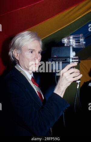 Andy Warhol with new Polaroid Polavision movie camera at an art opening in 1977. Warhol was an American visual artist, film director, producer, and leading figure in the pop art movement. His works explore the relationship between artistic expression, advertising, and celebrity culture that flourished by the 1960s, and span a variety of media, including painting, silkscreening, photography, film, and sculpture. Some of his best-known works include the silkscreen paintings Campbell's Soup Cans  and Marilyn Diptych. Photo by Bernard Gotfryd Stock Photo