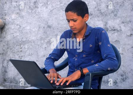Teen handsome student using laptop. Cheerful boy studying online on laptop. Technology, communication, social media, day time Stock Photo