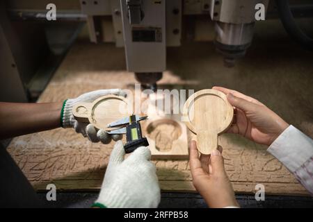 Female supervisor and CNC machine operator measuring cut out product with caliper. Stock Photo