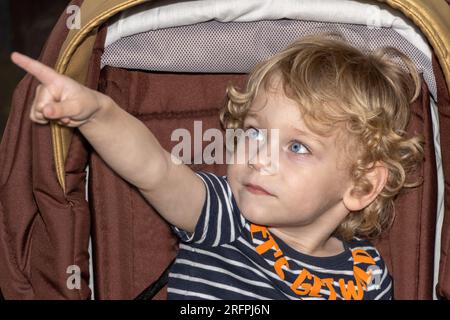 A little boy is sitting in a pram and pointing with his finger Stock Photo