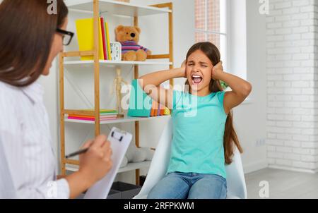 Autistic girl screaming and closing her ears during psychotherapy Stock Photo