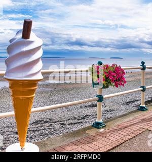 Giant plastic ice cream cone on seafront promenade on a cloudy afternoon. Mr Whippy. Flowers. Pavement. 99 Flake. Stock Photo