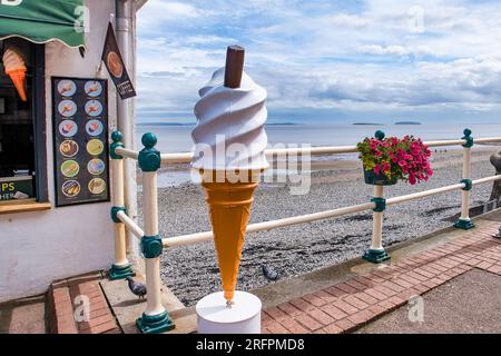 Giant plastic ice cream cone on seafront promenade on a cloudy afternoon. Mr Whippy. Flowers. Pavement. 99 Flake. Stock Photo