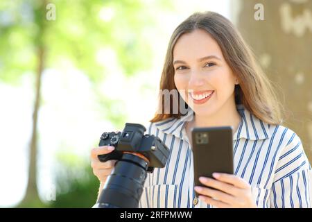 Happy photographer holds camera and smart phone posing looking at you in nature Stock Photo