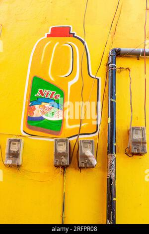 Advertisement painted on a yellow wall. Electric meters and evacuation pipe. Jinja, Uganda. Stock Photo