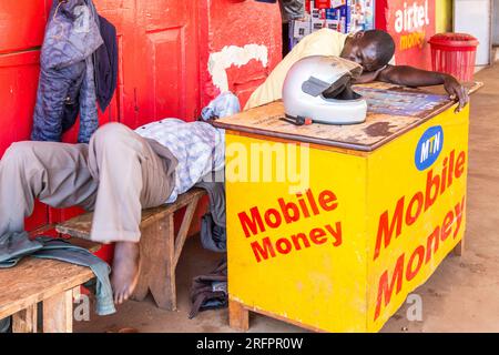 Two men asleep behind the counter of a stall. Jinja, Uganda. Stock Photo