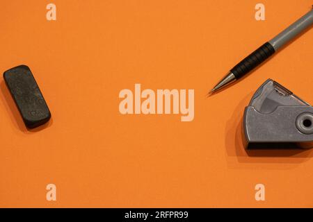 Pencil, pencil sharpener and an eraser isolated on an orange background with copyspace (aka empty text space). School background. Stock Photo