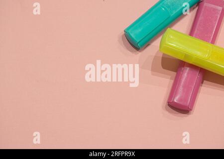 Three marker pens (pink, green and yellow) isolated on a pink background with copyspace (aka empty text space). School background. Stock Photo