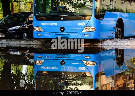 urban street scene in Budapest after heavy storm. passenger bus driving through deep storm water on flooded road. torrential rain concept. reflections Stock Photo