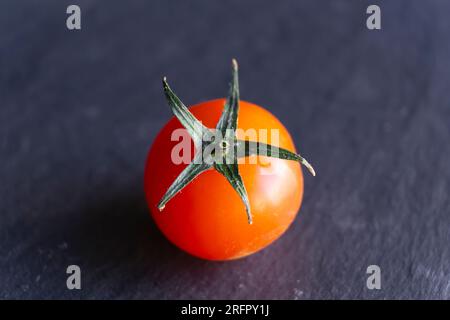 Top view close-up shot of a red cherry tomato isolated on dark blue background. Stock Photo