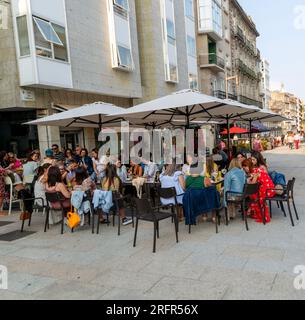 A large group of people sitting around  table at street cafe bar in the old town city centre of Vigo, Galicia, Spain Stock Photo