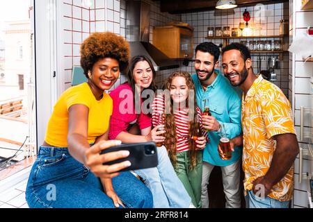 Multiethnic group of happy young friends having dinner barbecue party on rooftop at home - Multiracial cheerful young adult people having fun and bond Stock Photo