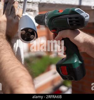 Man with a drill installing security cameras for surveillance in a house. Stock Photo