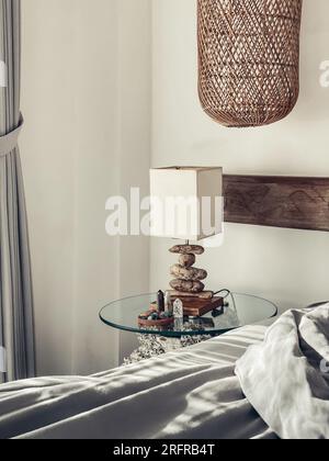 Bedside table with night light, different healing crystals and wicker hanging lamp in the bedroom Stock Photo