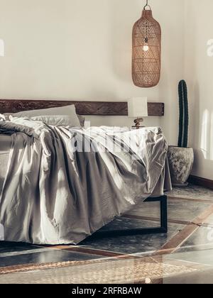 Loft style bedroom with gray bed linen set, hanging wicker lamps and bedside table Stock Photo