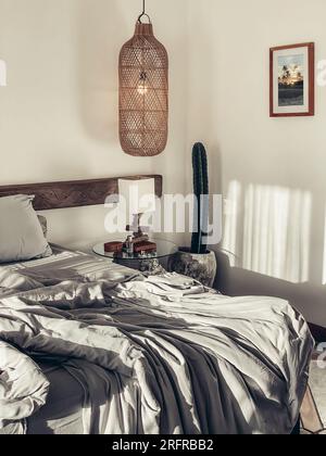 Loft style bedroom with gray bed linen set, hanging wicker lamps and bedside table. The photo in the frame was taken by me. Stock Photo
