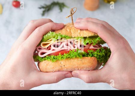 Sandwich. Man holding in his hands tasty sandwich with ham or bacon, cheese, tomatoes, lettuce and grain bread on dark backgrounds. Delicious club san Stock Photo