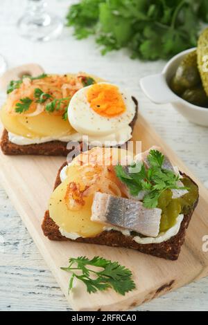 Open sandwich or smorrebrod with rye bread, herring, eggs, caramelized onions, parsley and cottage cheese on old wooden rustic table backgrounds. Dani Stock Photo