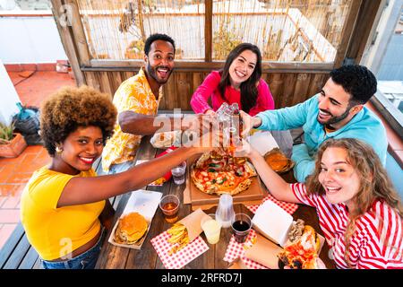 Multiethnic group of happy young friends having dinner barbecue party on rooftop at home - Multiracial cheerful young adult people having fun and bond Stock Photo