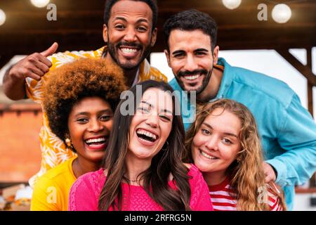 Multiethnic group of happy young friends having dinner barbecue party on rooftop at home - Multiracial cheerful young adult people having fun and bond Stock Photo