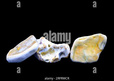 A group of three small stones collected from a beach. Negative space above. Black background. Brown, orange, yellow, white, purple. Stock Photo