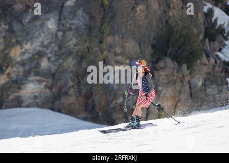 Mammoth Lakes, CA. July 4, 2023. A woman in patriotic American attire and a straw hat skis in front of a cliff  at Mammoth Mountain Ski Resort on a cl Stock Photo