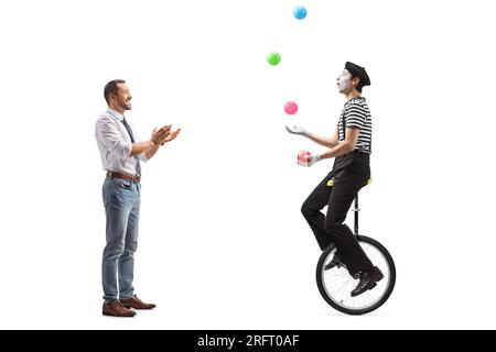 Full length profile shot of a man giving an applause to a mime on a unicycle juggling with balls isolated on white background Stock Photo