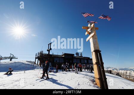 Mammoth Lakes, CA. July 4, 2023. American flags wave in sunshine as skiiers pass by  at the top of Mammoth Mountain Ski Resort on a clear summer day. Stock Photo