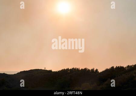 Colera, Spain. 05th Aug, 2023. A person looks down from the opposite mountain at the Colera fire at dawn enveloped in a cloud of smoke. A fire broke out in Portbou and Colera (Girona, Catalonia, Spain) on Friday 4 August, forcing residents to be confined to their homes. It is estimated that a total of 573 hectares have been affected. (Photo by Ximena Borrazas/SOPA Images/Sipa USA) Credit: Sipa USA/Alamy Live News Stock Photo