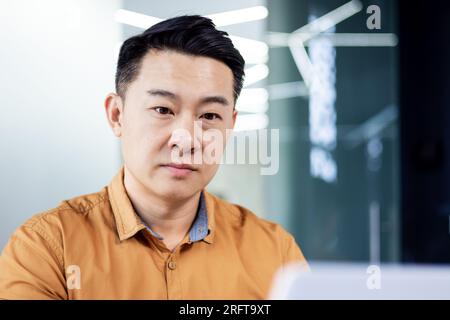 Thinking serious asian businessman working inside office at workplace, man looking concentrated at laptop screen, financier investor reading traders market. Stock Photo