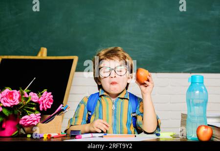 Little schoolboy in glasses eating apple at lunch time. Healthy breakfast. Delicious food for lunch. Primary school kid eat lunch in classroom Stock Photo