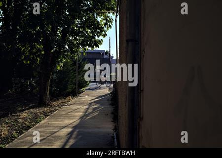 Gravel  path in a park next to a building that leads to a pedestrian crossing on a country road at sunset Stock Photo