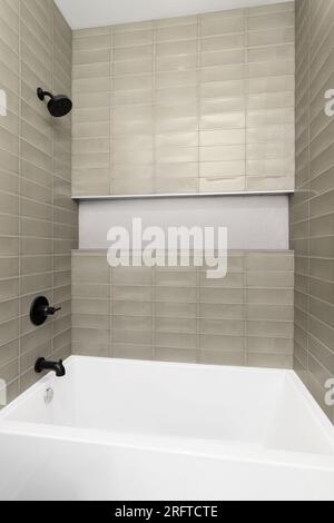 A shower with brown subway tile walls, small hexagon tiles in the shelf, and black shower head and faucet. Stock Photo