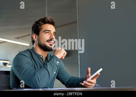 Thoughtful young Latin business man using mobile phone at work in office. Stock Photo
