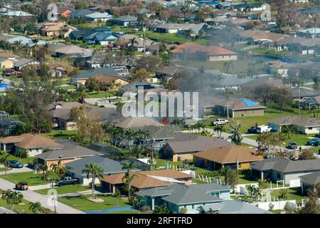 View from above of burning private house on fire and firefighters extinguishing flames after short circuit caused to ignite roof damaged by hurricane Stock Photo