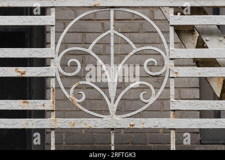 detail close up of wrought iron grate painted white on the side of fire escape with a decorative art deco medallion and peeling, rusting paint makes a Stock Photo