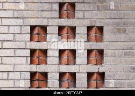two tone art deco decorative brick pattern in wall of beige bricks with inserts of terra cotta color bricks in a sawtooth placement create a geometric Stock Photo