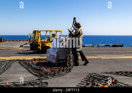 U.S. Marines and Sailors commence cargo transfer during a replenishment at sea aboard the Wasp-class amphibious assault ship USS Bataan (LHD 5), Mediterranean Sea, Aug. 4, 2023. In order to carry out any mission effectively, fleet units must be capable of remaining at sea for prolonged periods time and remain fully ready to carry out any assigned tasks. The 26th Marine Expeditionary Unit (Special Operations Capable) is embarked with the Bataan Amphibious Ready Group, continues to remain ready, relevant and capable across the Marine Air-Ground Task Force while on a scheduled deployment as the T Stock Photo