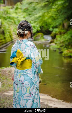 Back view of one woman wearing Japanese yukata summer kimono standing next to a river in Kyoto nature forest. Kyoto, Japan. Stock Photo