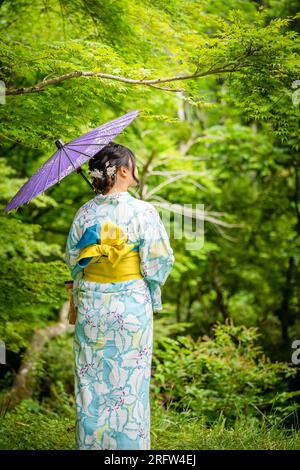 Back view of one woman wearing Japanese yukata summer kimono and holding Japanese traditional oil paper umbrella in nature forest. Kyoto, Japan. Stock Photo